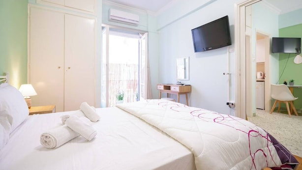 A hotel room with a bed, a desk, a chair, a TV, and an air conditioning unit.