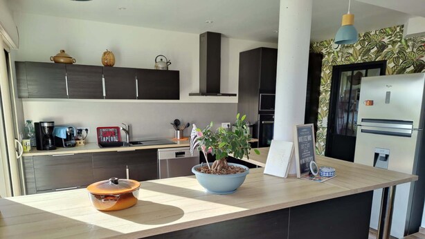 Een moderne keuken met donkere kastjes, een houten aanrecht, een koffieapparaat, een waterkoker, een potplant en een koelkast.