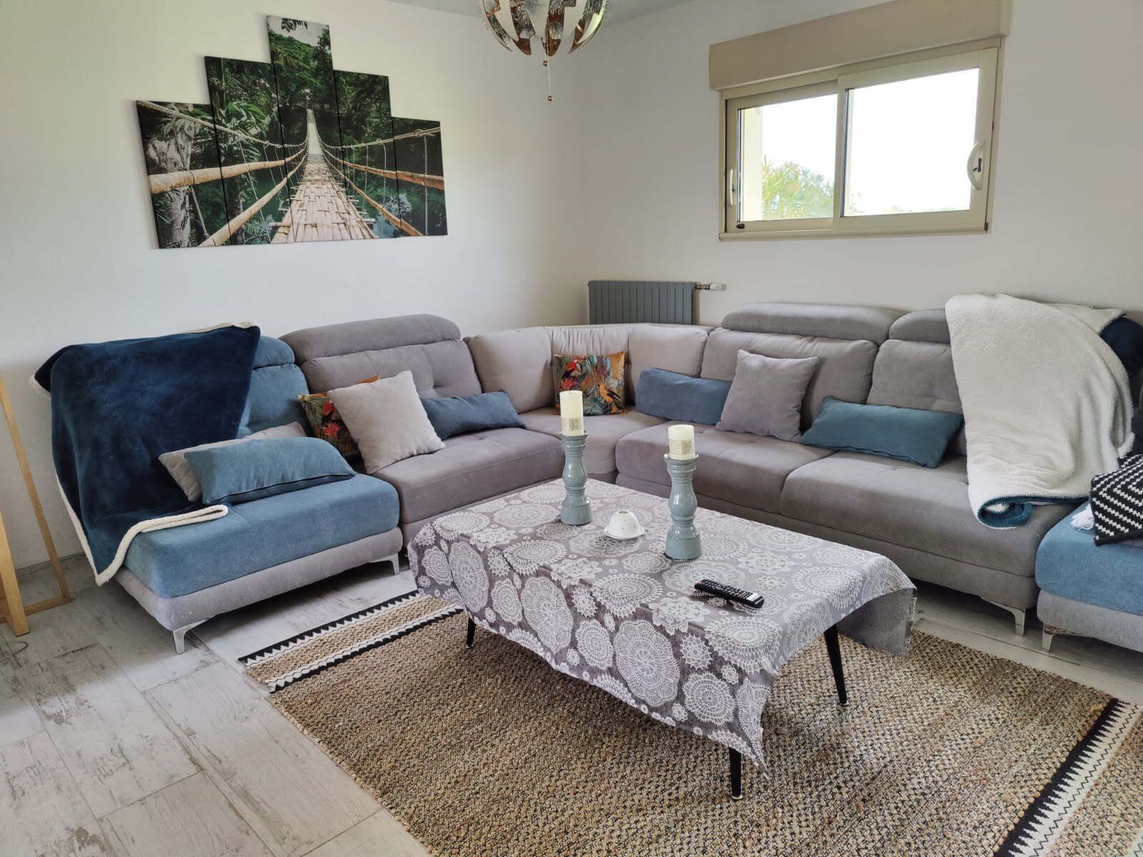 Ein Wohnzimmer mit einer Sofagarnitur, einem Couchtisch mit Kerzen, einem Teppich und einem Gemälde einer Brücke.