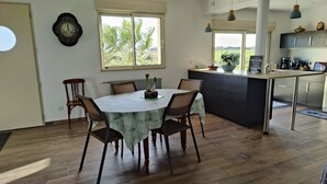 Een moderne keuken met een eethoek, met een ronde tafel met stoelen, een klok aan de muur en uitzicht op het landschap door grote ramen.