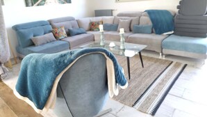 Een moderne woonkamer met een modulaire bank, een glazen salontafel en een blauwe fauteuil.
