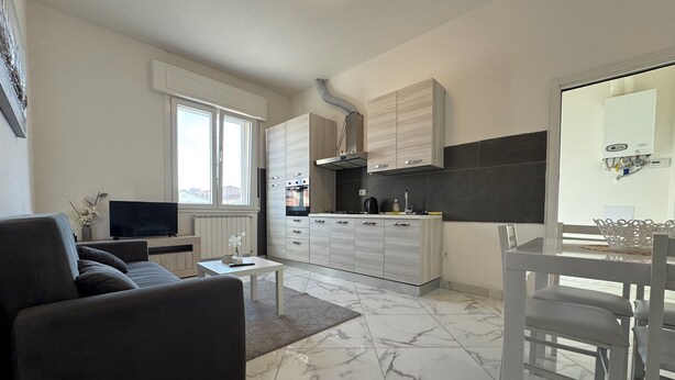 Una cucina moderna con mobili bianchi, forno integrato e zona pranzo con tavolo e sedie bianche.