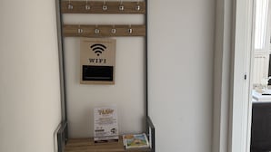 Un appendiabiti con ganci, un cartello di legno con il simbolo WiFi e un cartello di benvenuto in un corridoio.