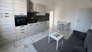 Una cucina moderna con forno a incasso e piano cottura, un'area pranzo con tavolo e sedie, e un soggiorno con divano e tavolino.