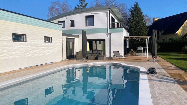 Una casa moderna con piscina, mobiliario exterior y un patio cubierto.