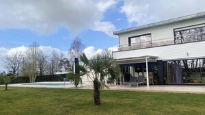 Una casa moderna de dos pisos con un porche cubierto, una piscina y un césped bien cuidado.