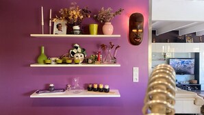 Una habitación con paredes moradas, estantes decorados con diversos objetos, un televisor y una máscara decorativa.