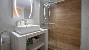 Une salle de bain moderne avec une douche à parois de verre, un meuble-lavabo blanc avec un miroir et un plancher en bois.