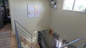 Un escalier avec une rampe en métal mène au deuxième étage. Une fenêtre offre une vue sur la verdure environnante.