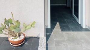 Une entrée d’immeuble avec un cactus en pot, un panneau indiquant le numéro de l’immeble, et un sol carrelé.