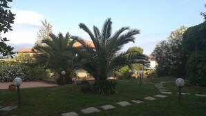 Un jardin avec un chemin dallé, des palmiers et des luminaires sphériques.