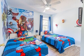 Een hotelkamer met twee bedden, een plafondventilator, een televisie en een grote muurschildering met superhelden.