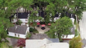 Vista aérea de un barrio residencial con casas numeradas, un patio central con mobiliario exterior y zonas verdes circundantes.