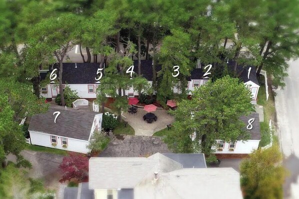 Vista aérea de un barrio residencial con casas numeradas, un patio central con mobiliario exterior y zonas verdes circundantes.