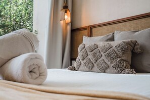 A neatly made bed with a rolled white towel, a textured pillow, and a headboard with a wooden frame. - Villa Sorella (Tulum)