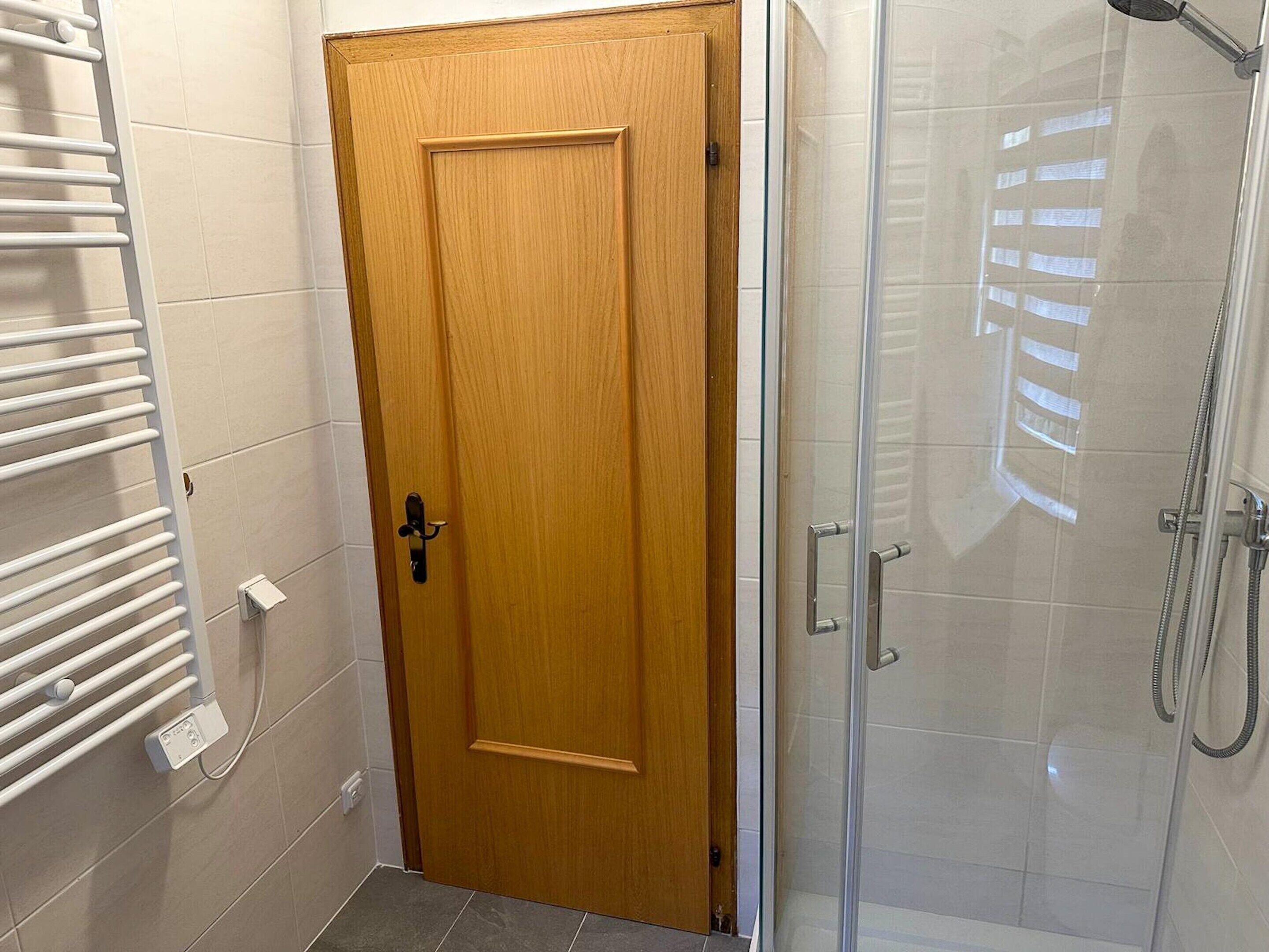 A bathroom with a wooden door, a glass shower enclosure, and a white towel rack.