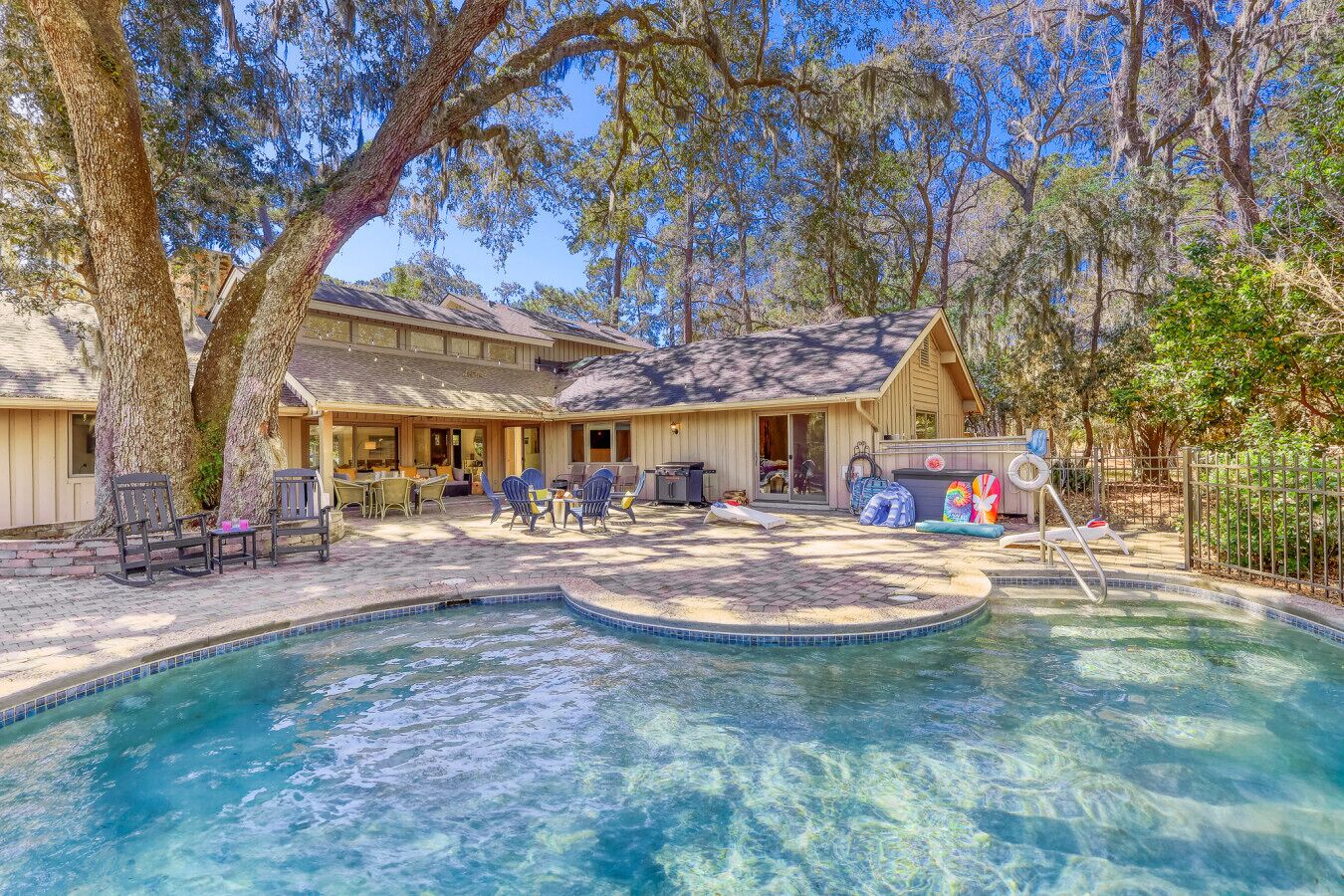 A backyard with a swimming pool, a covered patio with outdoor furniture, and a wooden house.