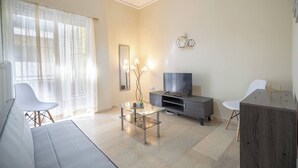 Een moderne woonkamer met een bank, een glazen salontafel, een televisie op een houten kast en een fauteuil.