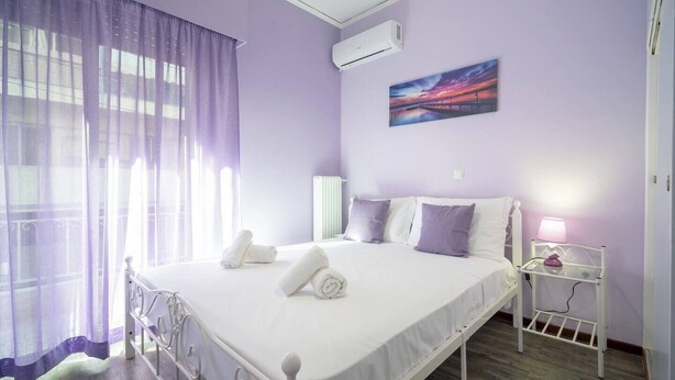 Een slaapkamer met een bed, nachtkastje, lamp en een schilderij aan de muur.