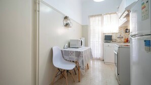 Een kleine keuken met een tafel, stoelen, een magnetron, een koelkast en een raam met gordijnen.