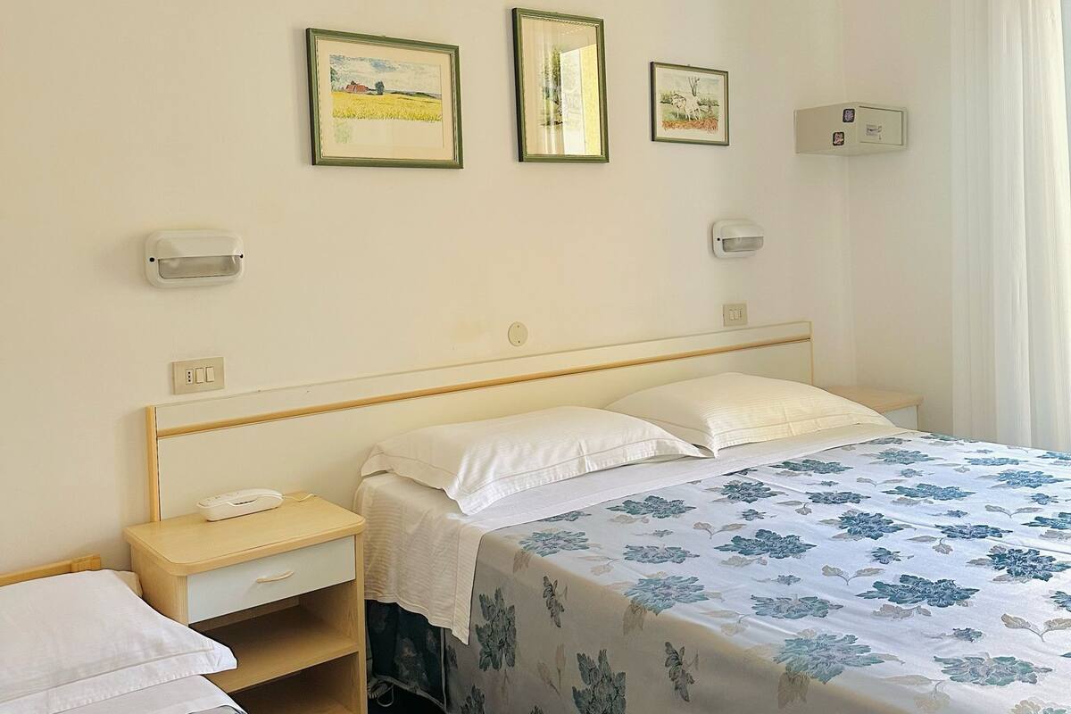 A bedroom with a single bed, a nightstand, and a bedside table. There are three framed pictures on the wall.