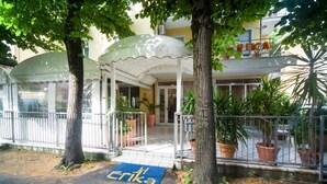 A hotel entrance with a covered porch, potted plants, and a blue mat with the hotel's name. - Hotel Erika (Rimini)