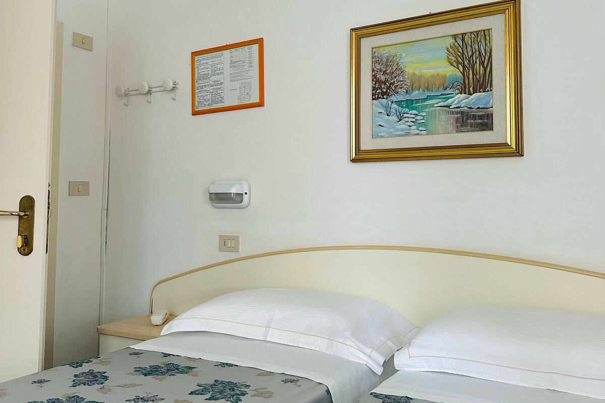 A hotel room with a bed, a door, a wall-mounted light, and a framed picture.