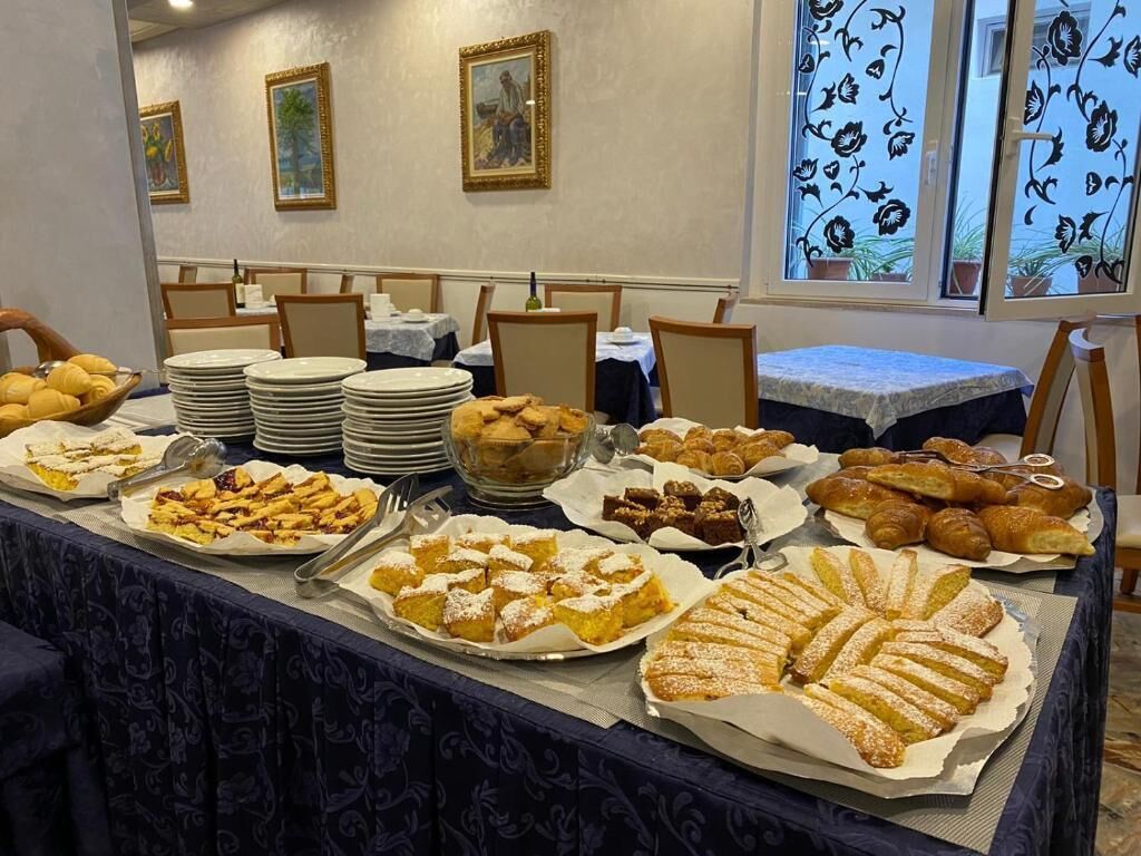A buffet table with various pastries and desserts, including croissants, muffins, and fruit tarts, set up in a dining area with chairs and tables.