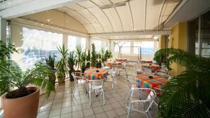 A covered patio area with tables and chairs, surrounded by potted plants. - Hotel Erika (Rimini)
