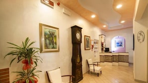 A lobby with a reception desk, chairs, a large clock, and framed artwork on the walls. - Hotel Erika (Rimini)