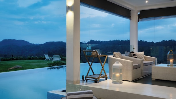 A modern outdoor lounge area with a pool, wicker furniture, and a view of the hills. - Camelia Ranch (Baddegama)