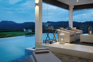 A modern outdoor lounge area with a pool, wicker furniture, and a view of the hills.