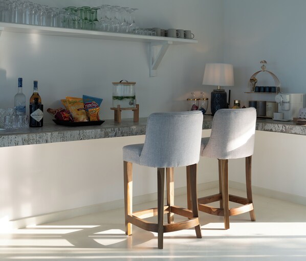 A modern kitchen with two bar stools, a coffee machine, and a shelf with glassware and snacks.
