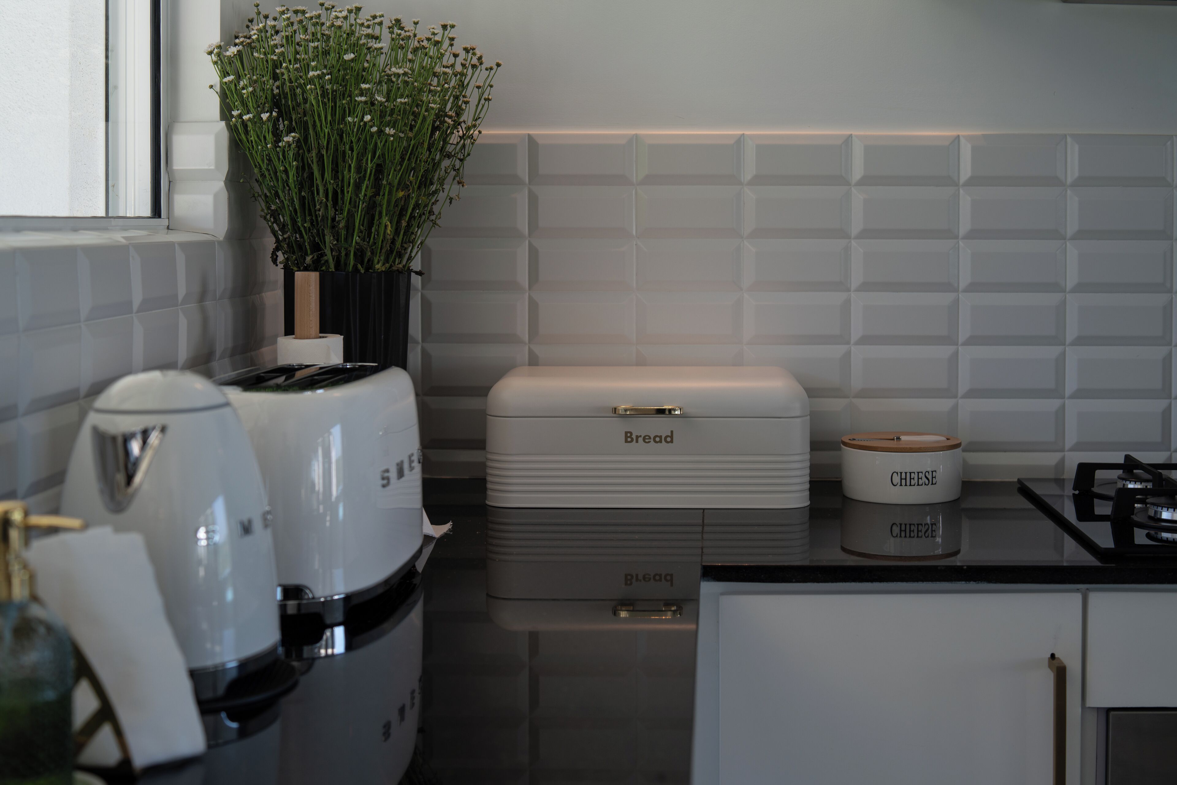 A kitchen with a bread box, a cheese container, and a potted plant.