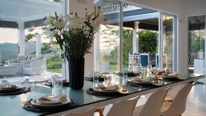 A modern dining area with a glass table, white chairs, and a vase of flowers. - Camelia Ranch (Baddegama)