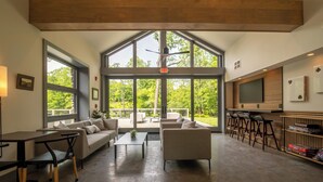 A spacious indoor area with large windows, a sofa set, a coffee table, and a bar area with stools. - 3-bedroom luxury home with Catskill charm (Livingston Manor)