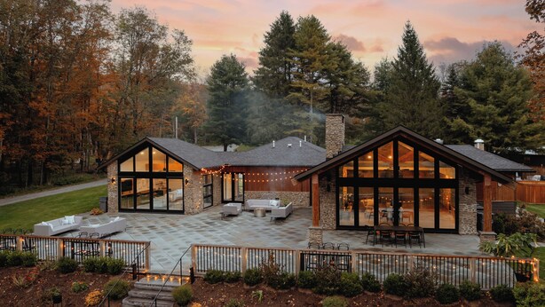 A modern house with a patio area, large windows, and a stone chimney. - 3-bedroom luxury home with Catskill charm (Livingston Manor)