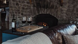 A cozy room with a stone wall, a fireplace, a bed with a striped blanket, and a wine bottle on a table. - 3-bedroom luxury home with Catskill charm (Livingston Manor)