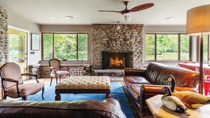 A cozy living room with a stone fireplace, leather furniture, and large windows offering a view of the outdoors. - 3-bedroom luxury home with Catskill charm (Livingston Manor)