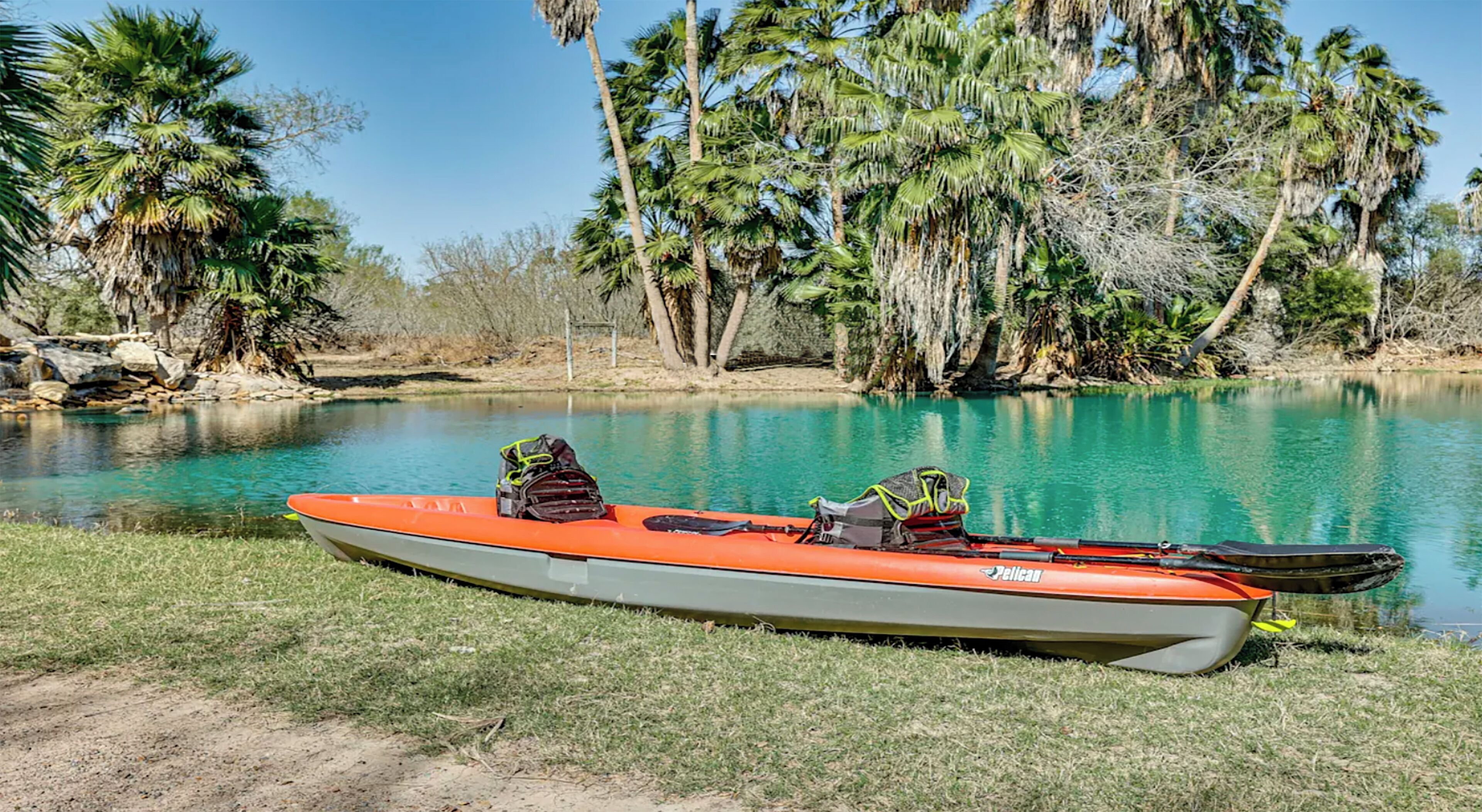 Un barco amarrado en un río tranquilo, con una orilla cubierta de hierba y palmeras al fondo.