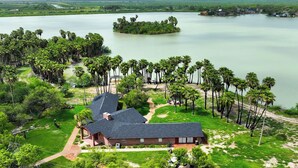 A house with a dark roof, surrounded by a lush green landscape and a calm lake. - Rancho El Charco Resort - Private Pool, Wildlife & Lake Retreat (La Joya)