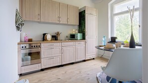 A modern kitchen with light wooden cabinets, a built-in oven, a microwave, and a dining area with a white chair and table. - Boarding & Fitter Apartment CMTZ (Chemnitz)