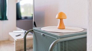 A small, green metal cart with a wooden mushroom decoration on top, placed in a room with a television in the background. - Boarding & Fitter Apartment CMTZ (Chemnitz)