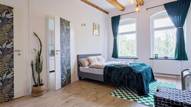 A bedroom with a bed, a checkered rug, a window with curtains, and a plant. - Boarding & Fitter Apartment CMTZ (Chemnitz)