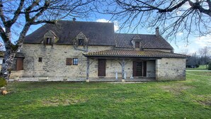 Ein Haus aus Stein mit Ziegeldach, einer kleinen Veranda und einem grünen Rasen.