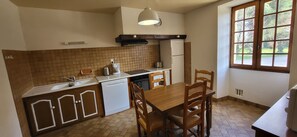A compact kitchen with a dining area, a built-in dishwasher, a refrigerator, and a window with a view of greenery. - LA BASTIDE.... Beautiful typical Périgord noir house (Saint-Genies)