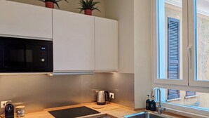 A modern kitchen with white cabinets, a black microwave, a built-in oven, a coffee maker, and a window with shutters. - Peaceful Roman Retreat (Roma)