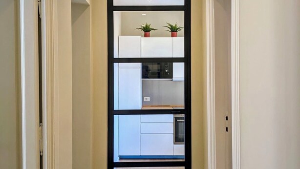 A narrow hallway with a modern kitchen area visible through a glass partition. - Peaceful Roman Retreat (Roma)