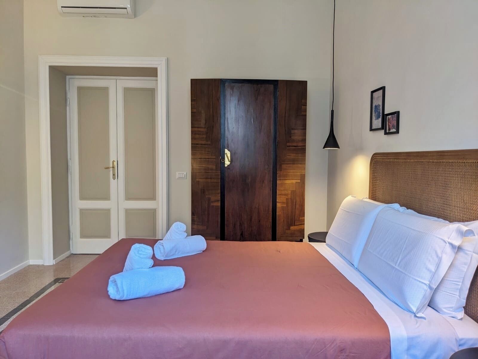 A hotel room with a bed, a wardrobe, a door, and a wall-mounted air conditioner.