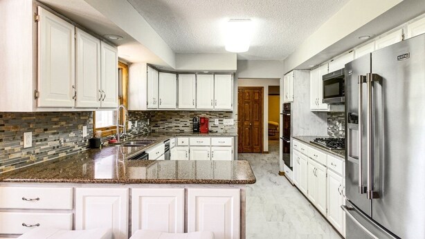Cozinha moderna com armários brancos, bancadas de granito, eletrodomésticos de aço inoxidável e uma ilha central com banquetas.
